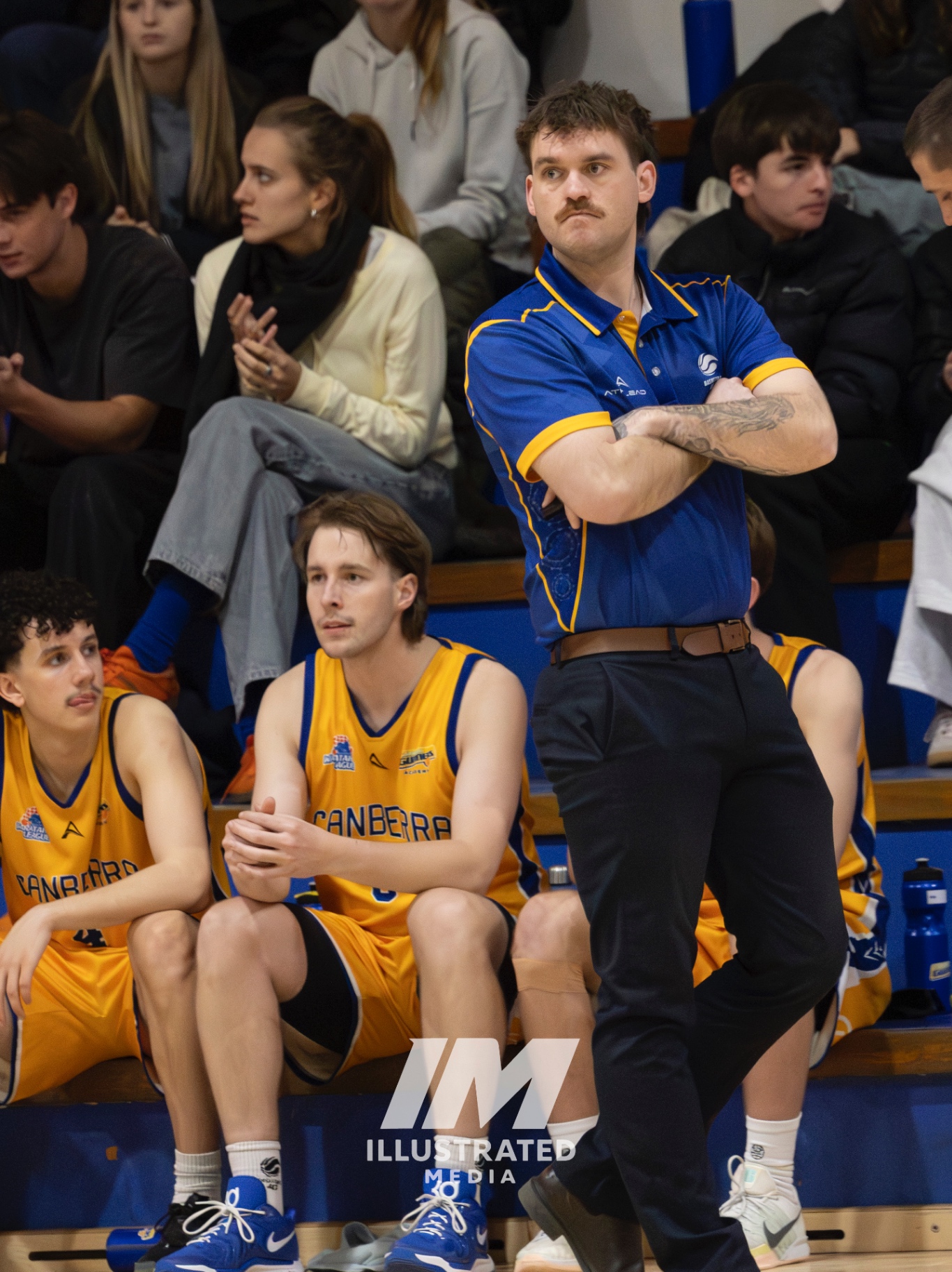 Coach standing on the sideline during a basketball game with players seated nearby.