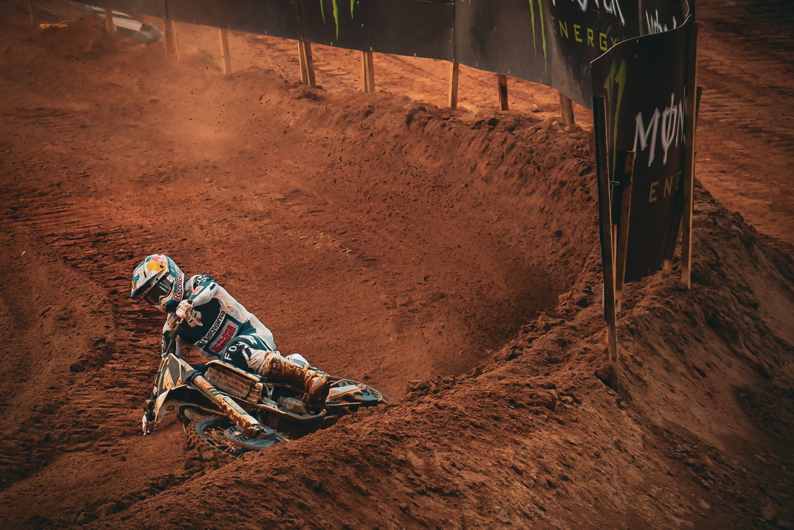 Motocross rider leaning low through a heavily rutted corner on a dirt track.